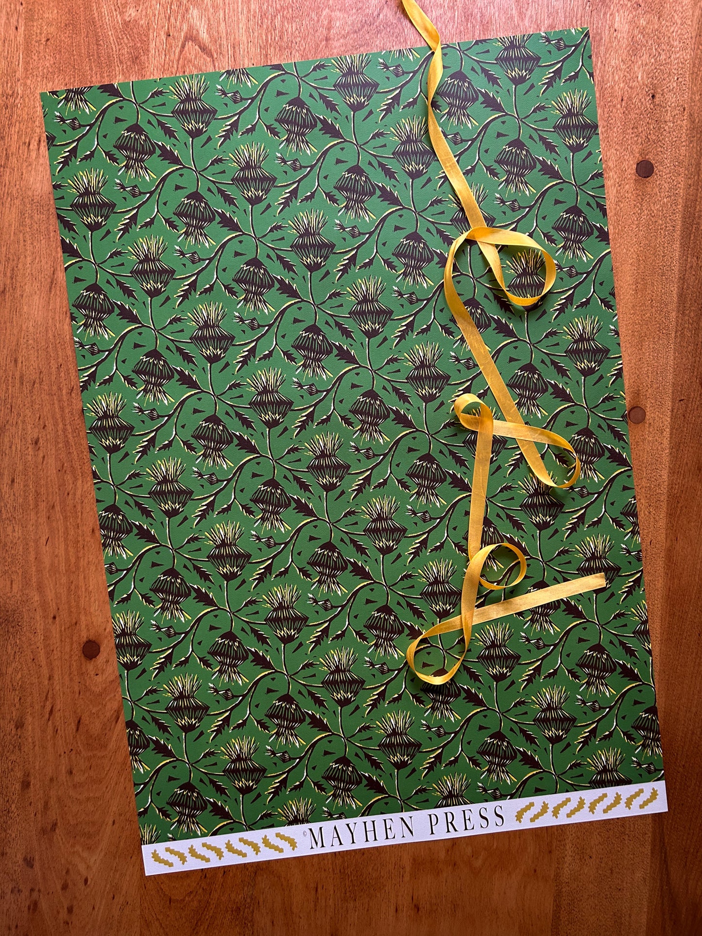 sheet of green thistle flower patterned crafting paper on a wooden background