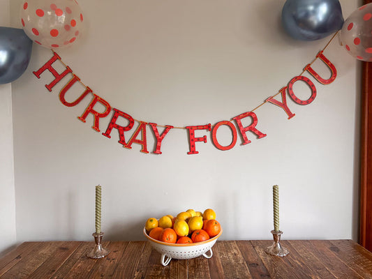 "Hurray For You" banner on wall hanging over a bowl of bright oranges and lemons with candle sticks on either side of the bowl