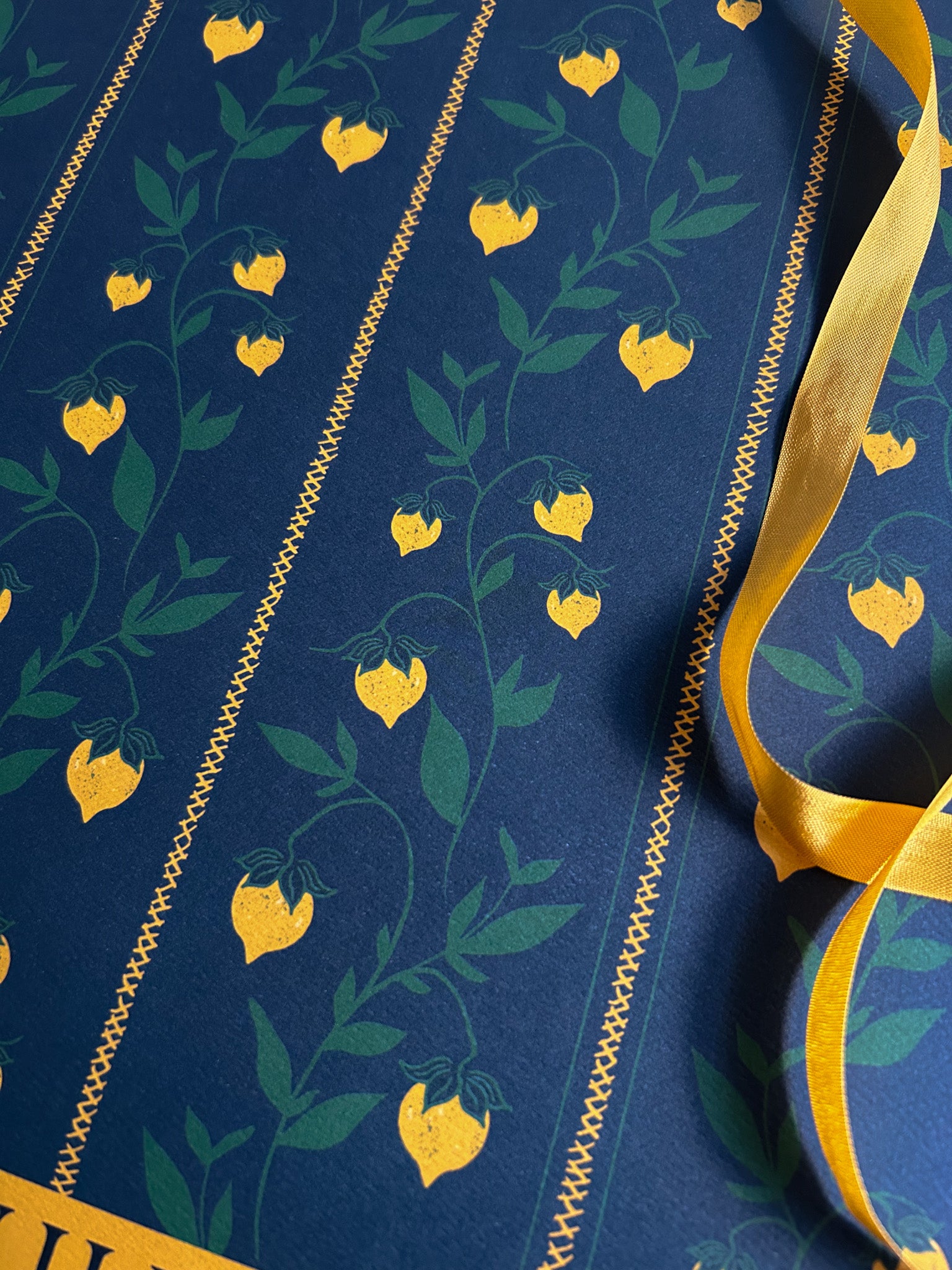 close up of a berry vine patterned wrapping paper sheet with yellow berries on a dark green background