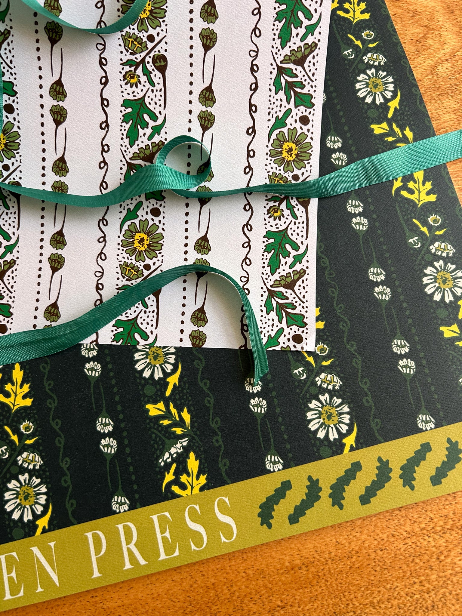 A double sided wrapping paper sheet with a floral pattern featuring chamomile flowers and leaves in shades of green and white. 