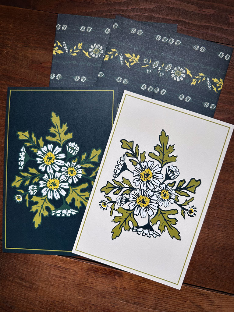 Two wildflower floral greeting cards with patterned envelopes on a wooden surface