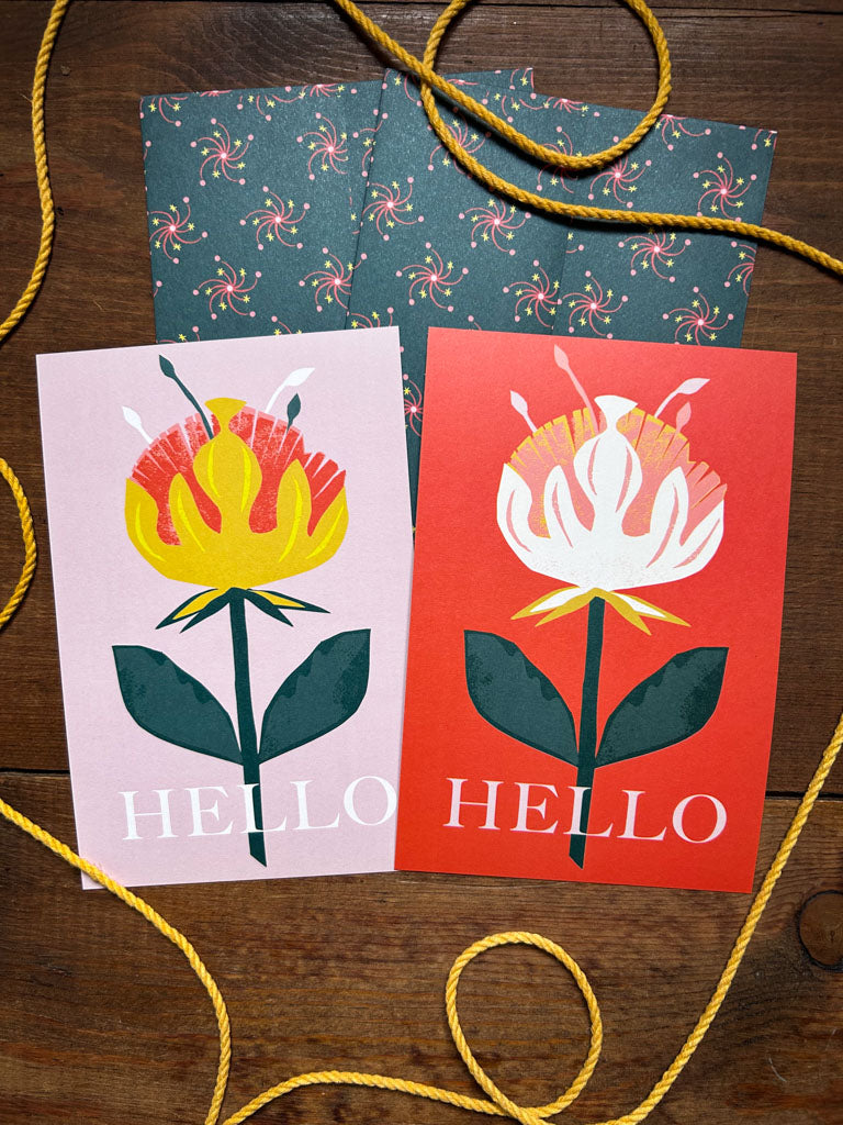 Colorful greeting cards with floral designs and 'HELLO' text with matching patterned envelopes on a wooden surface.