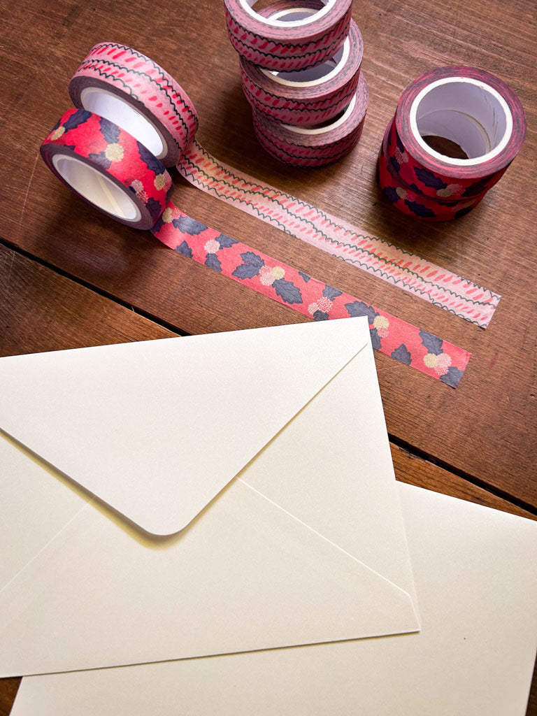 Decorative washi tape with floral and scallop pattern on a wooden surface with envelopes.