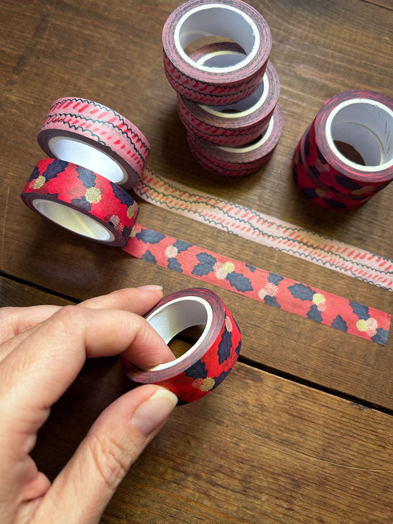 Decorative tape rolls on a wooden surface with a hand holding one roll.