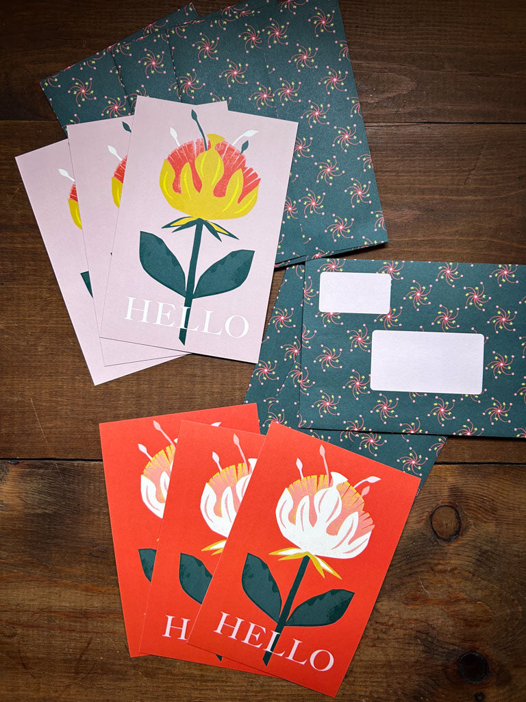 Colorful greeting cards with floral designs and 'HELLO' text with matching patterned envelopes on a wooden surface.