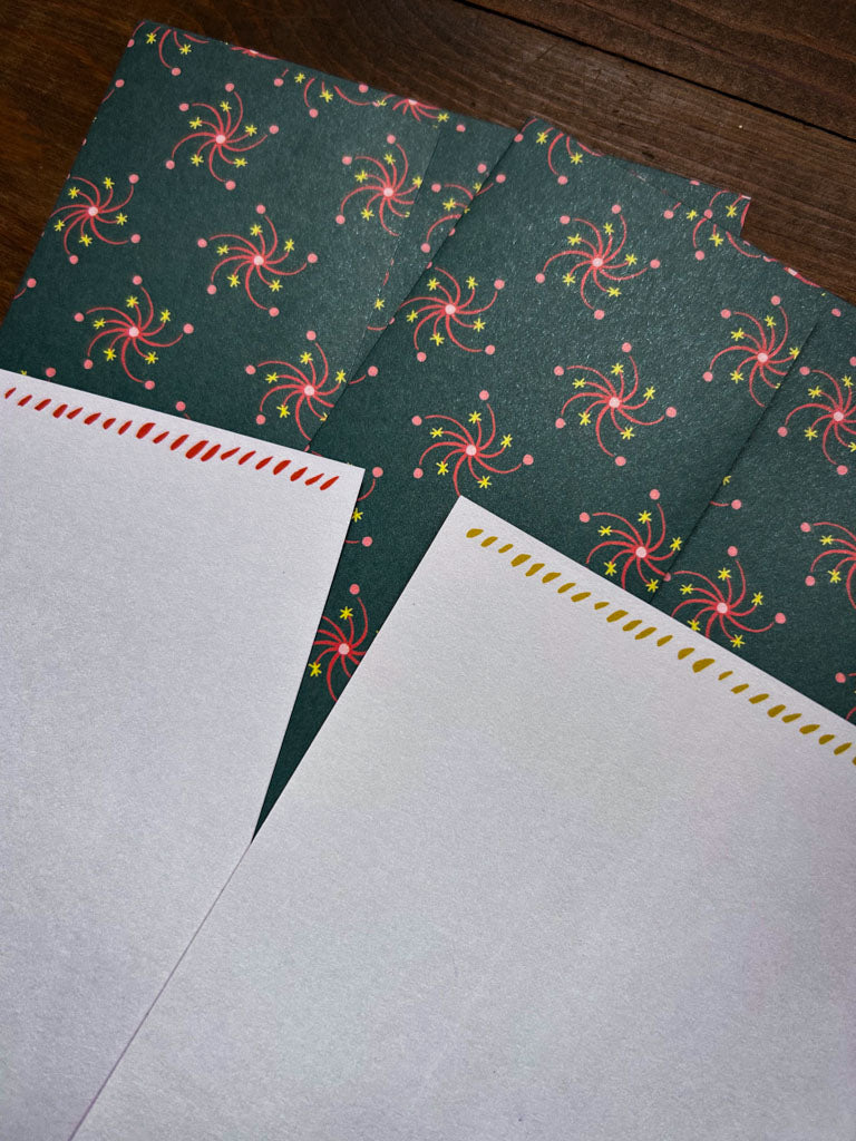 Two green patterned envelopes with pink floral patterns and the back side of two notecards on a wooden surface