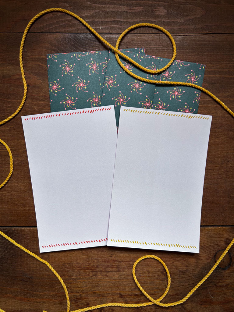 back side of two notecards with decorative edges and matching patterned envelopes on a wooden surface with yellow string.