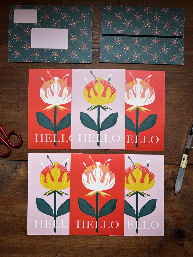 Colorful greeting cards with floral designs and 'HELLO' text with matching patterned envelopes on a wooden surface.
