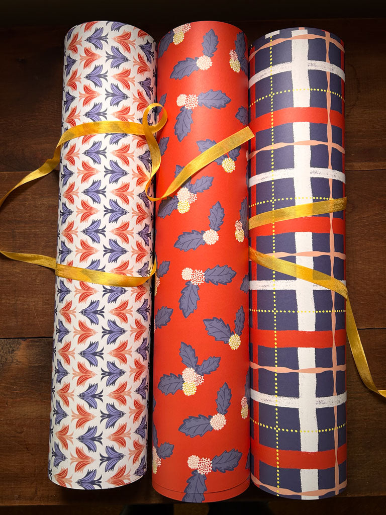 Three rolls of coordinating patterned paper tied with yellow ribbons on a wooden surface