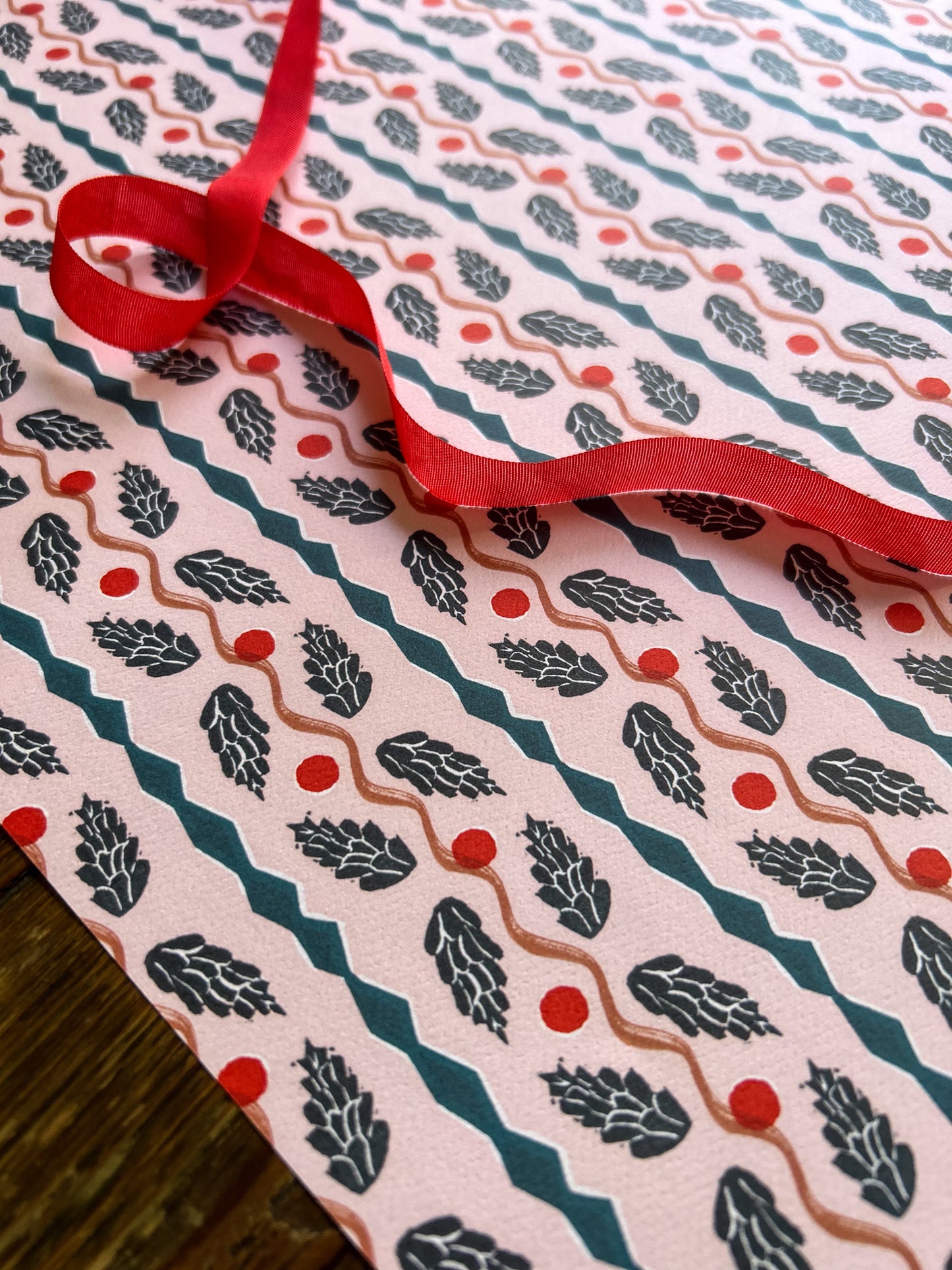 close up of a pinecone panel patterned wrapping and crafting paper sheet with blue pinecones on a light pink background