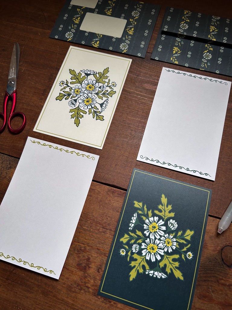 Floral stationery items in green and cream colors on a wooden surface 