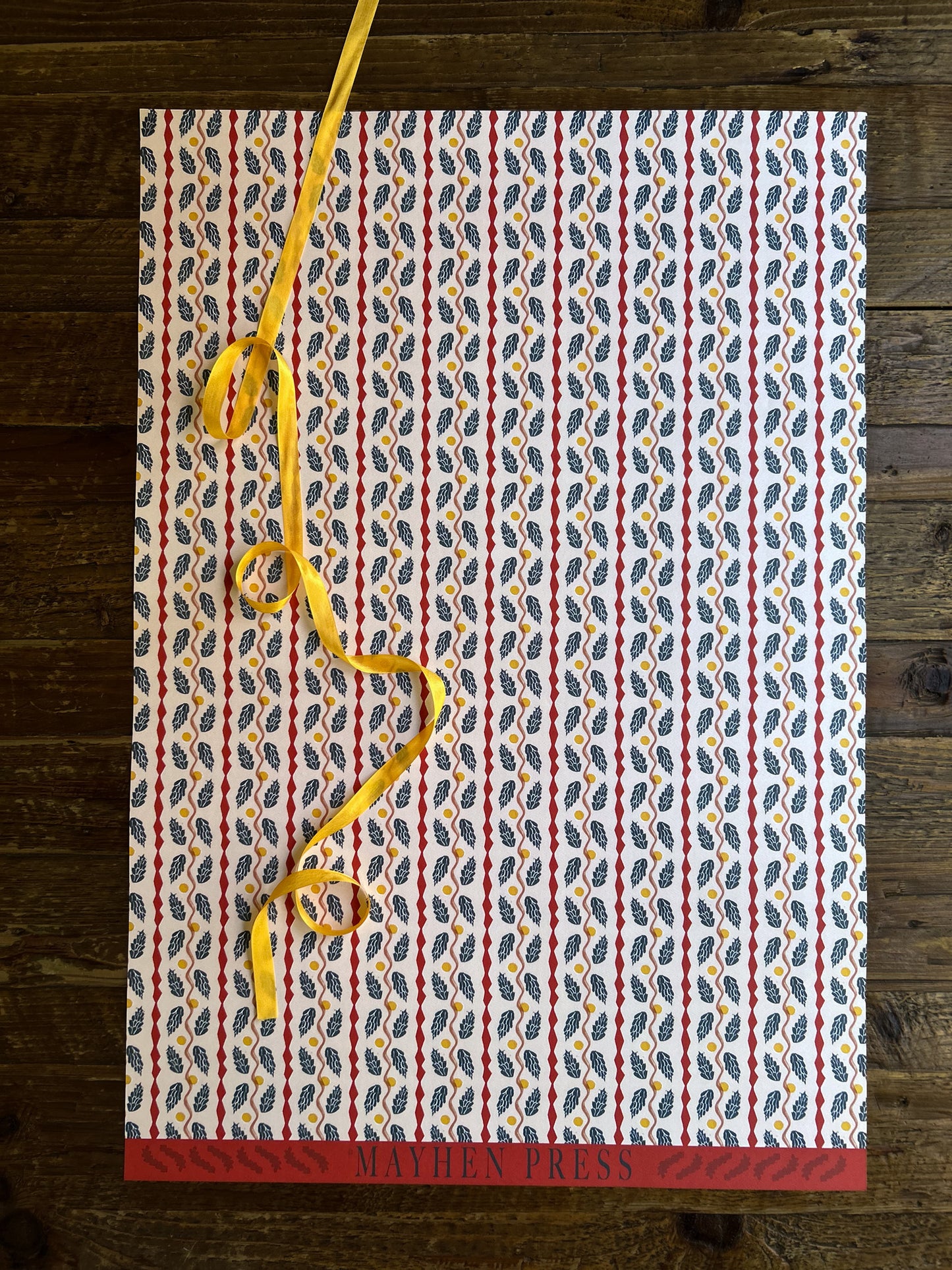 full sheet of pinecone patterned crafting paper on a wooden background featuring 'Mayhen Press' branding