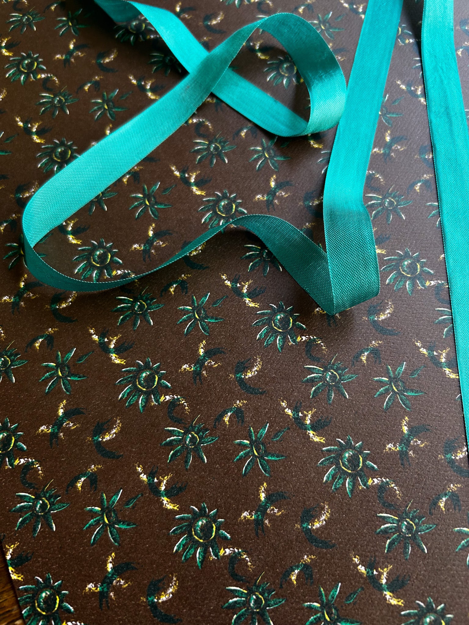 close up of daisy floral patterned wrapping paper with green flowers on a rich brown background